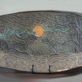 Handbuilt ceramic platter, carved with mountain landscape scene and sky, glazed in copper green glaze with accents in other oxides and glazes.
