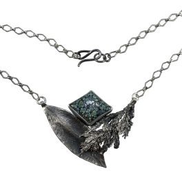 A necklace featuring a sterling silver mountain laurel leaf and cedar tip that cradle a variscite stone that looks like lichen.