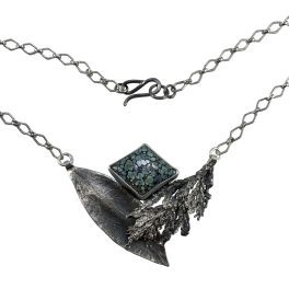 A necklace featuring a sterling silver mountain laurel leaf and cedar tip that cradle a variscite stone that looks like lichen.