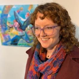 Artist Nicolette Yates smiling and standing in front of her painting "Rainbow Wrangler" at an art opening in Asheville.